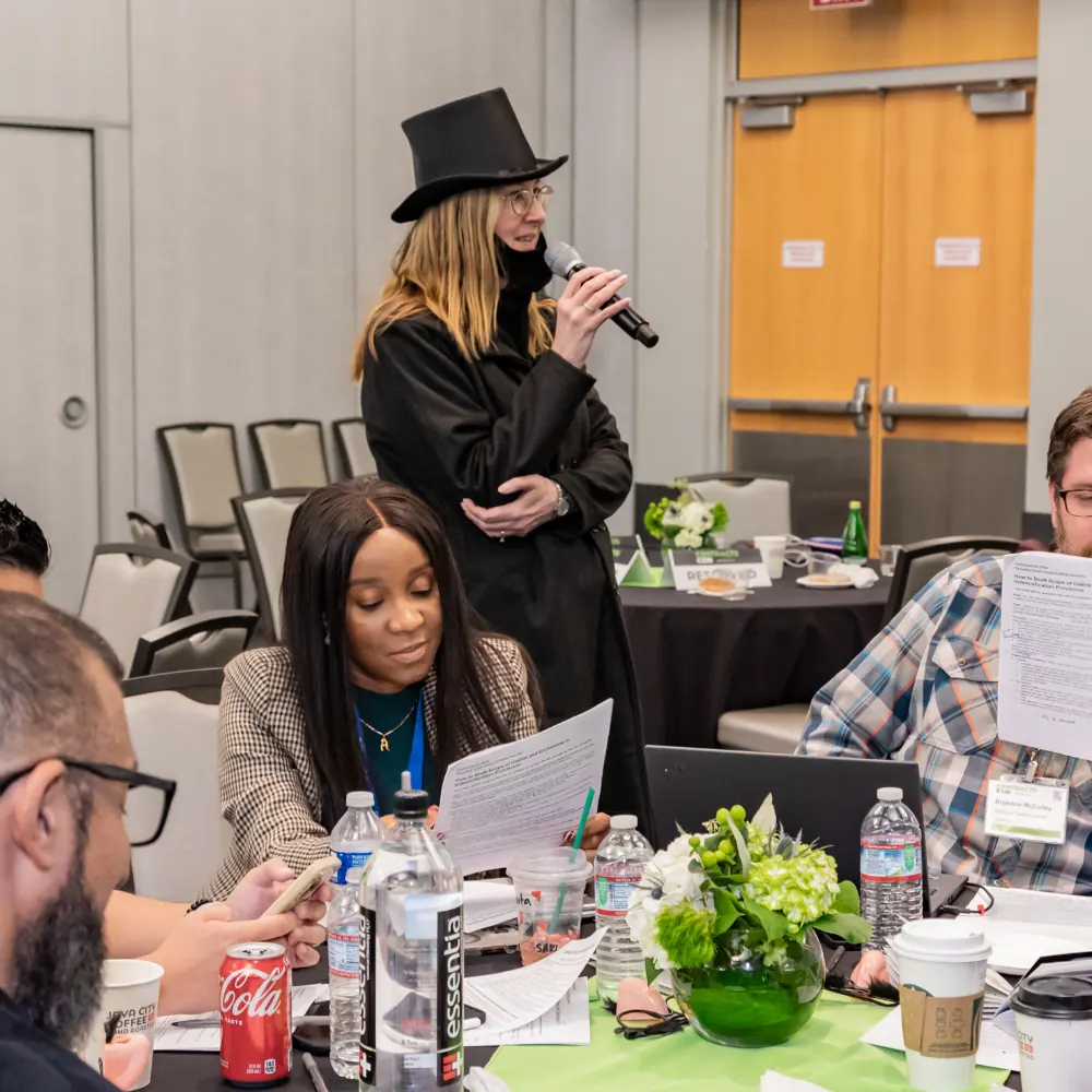 A ContractsCon speaker in a top hat leaning over a table, talking a group through contract language.