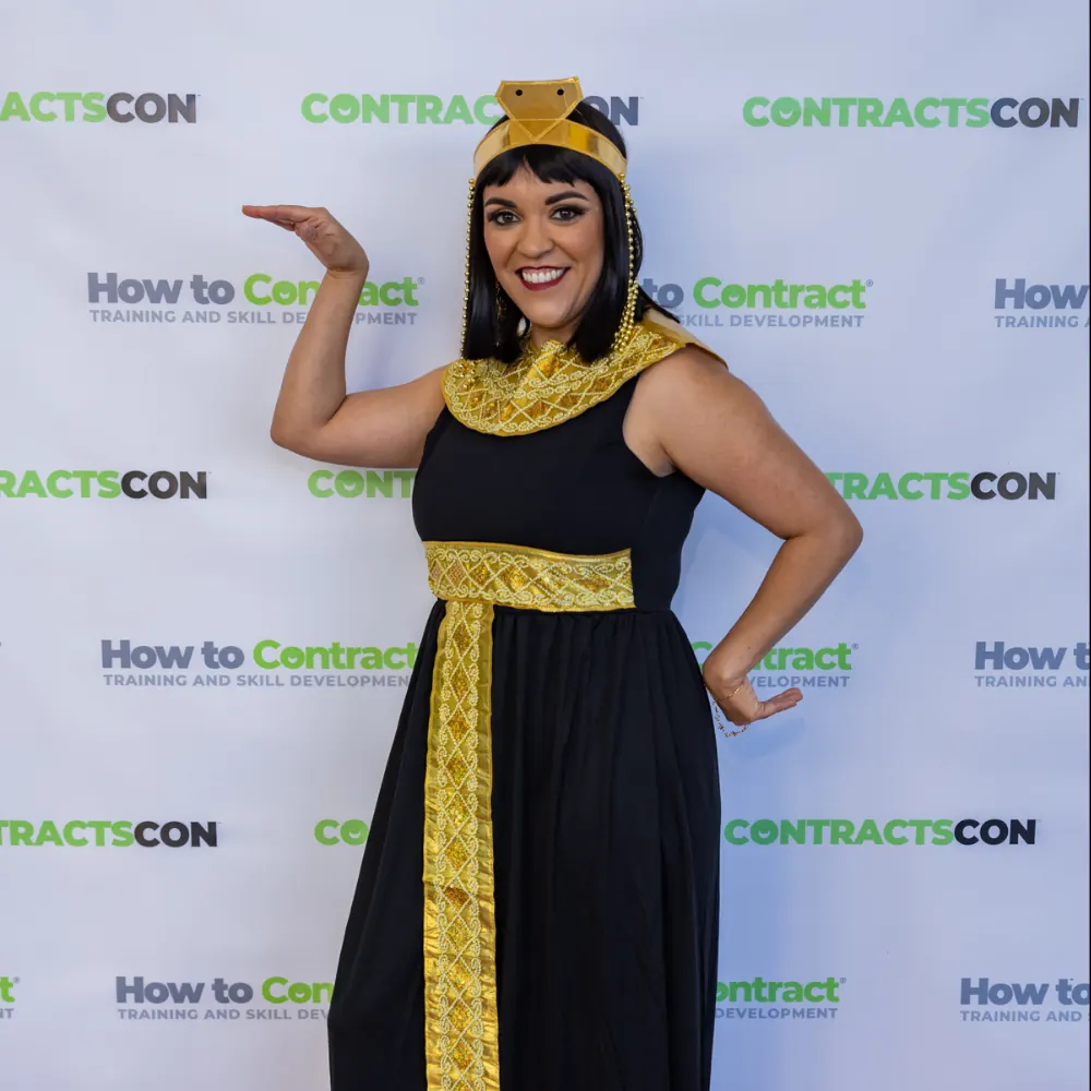 A speaker dressed as Cleopatra standing in front of the ContractsCon backdrop.