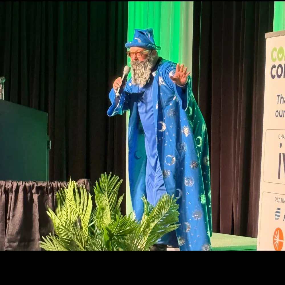 A speaker on stage in a blue wizard robe presenting a session slide.